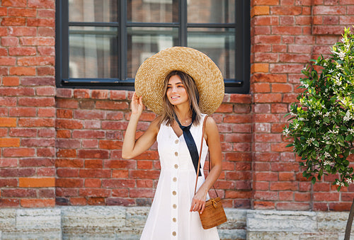 Stylish female with straw hat walking outdoors in front of a building