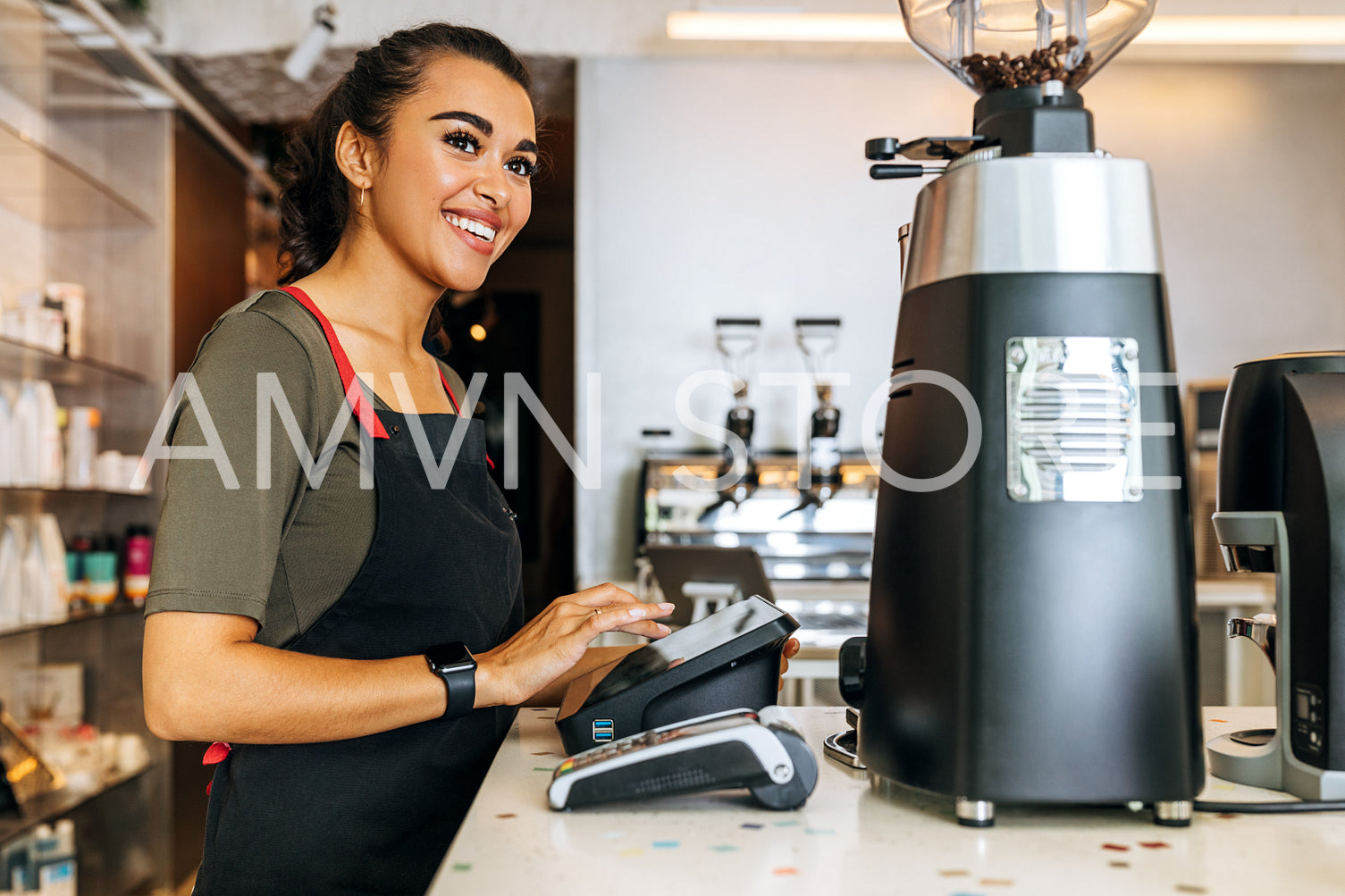 Female barista at counter using cashbox computer in coffee shop. Smiling waitress wearing apron and looking away.	