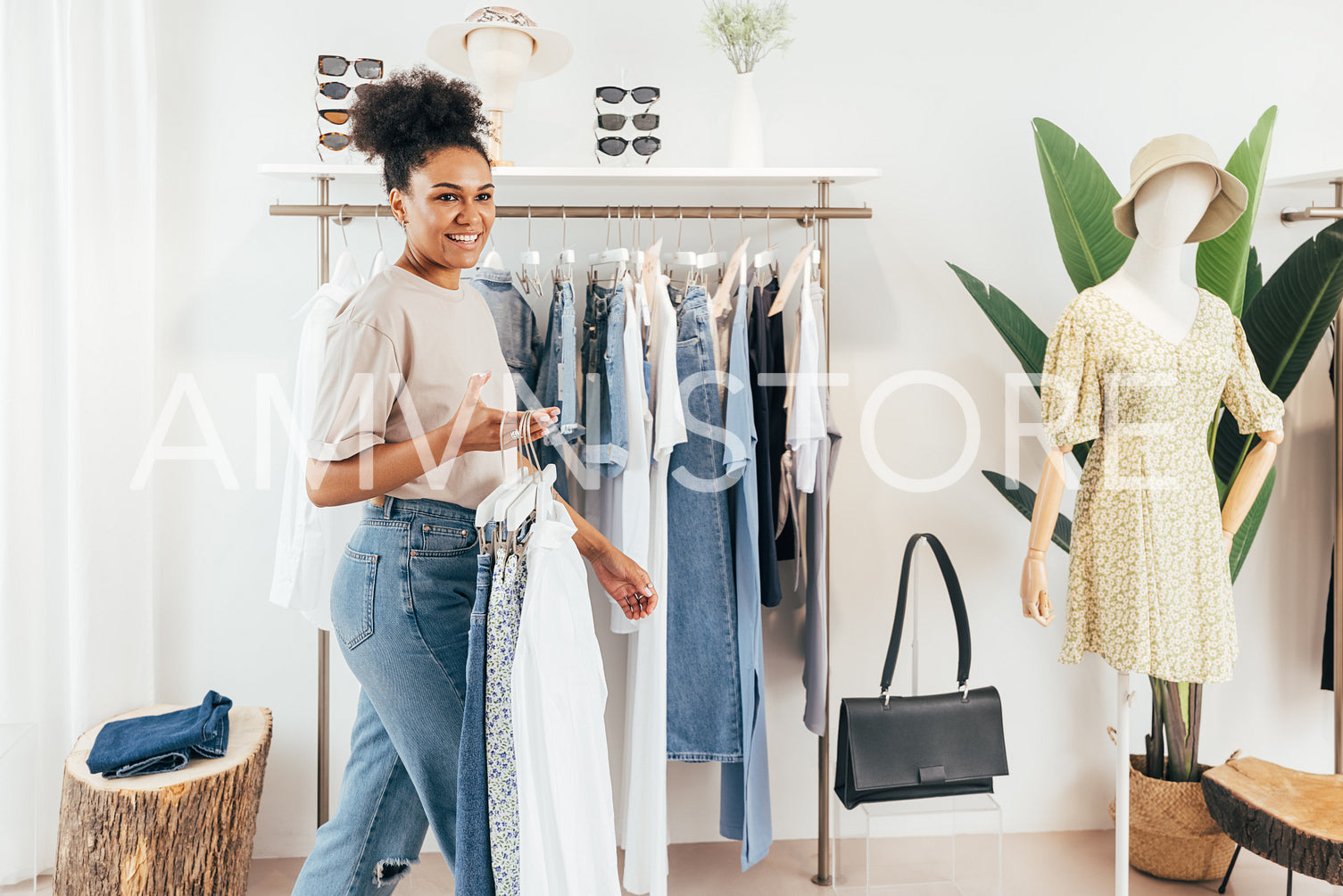 Woman working in a small fashion store, holding a bunch of hangers with clothes