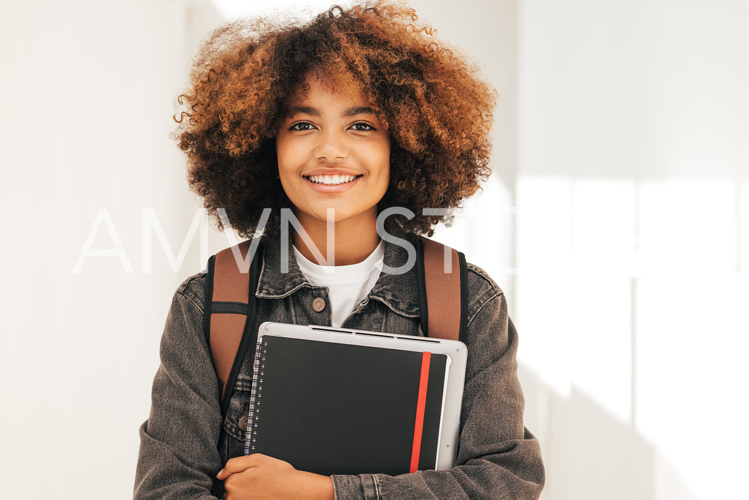 Close up portrait of a smiling student with textbook and laptop standing looking at camera