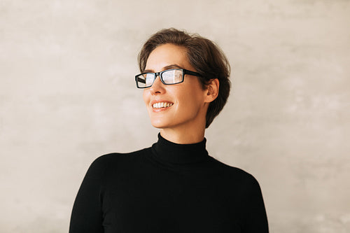 Portrait of a smiling businesswoman with short hair. Positive female in eyeglasses wearing black formal wear and looking away.