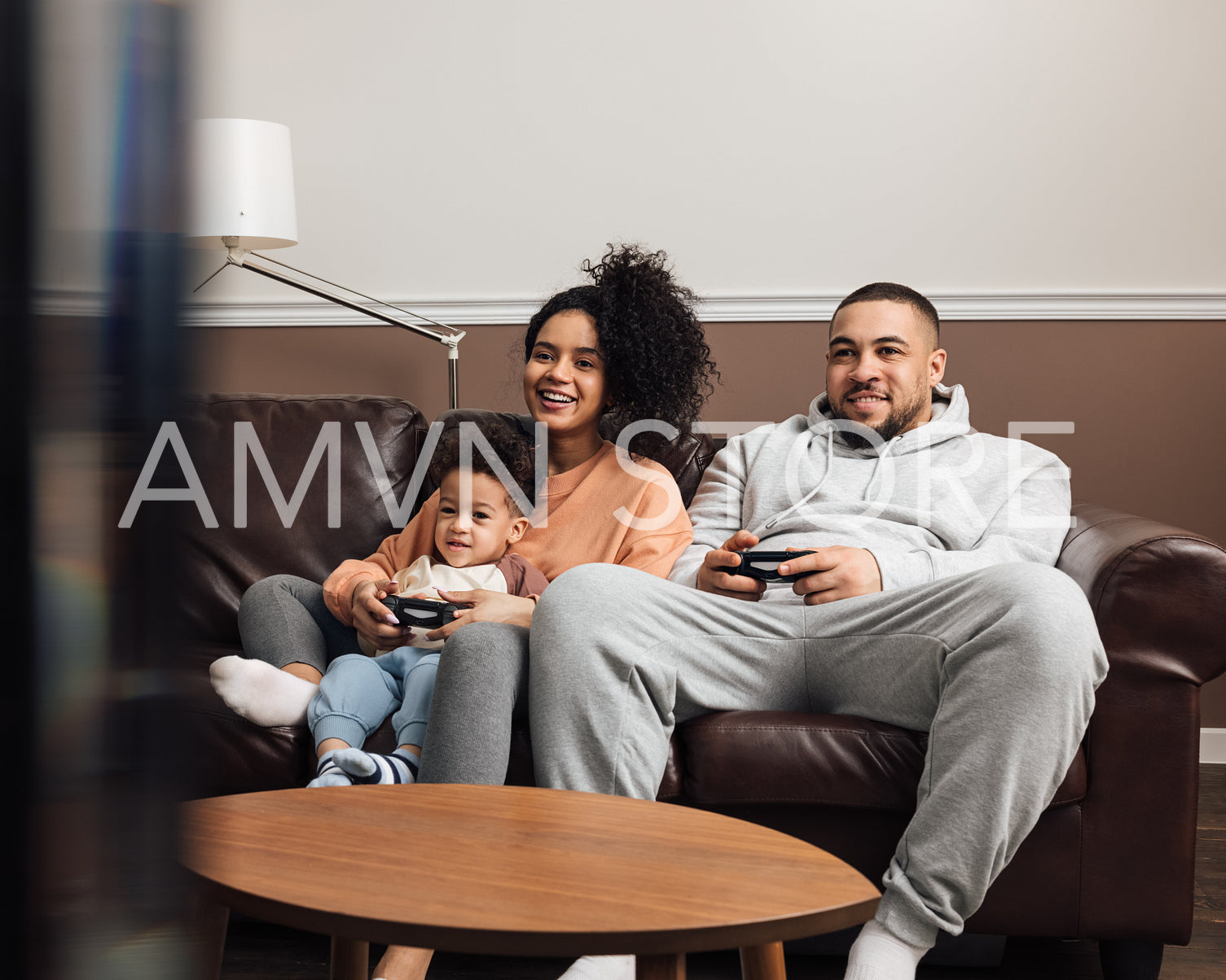 Mother, father and their little son playing video games while sitting on sofa at home