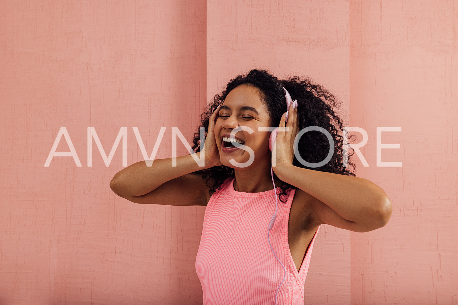 Young woman having fun while listening to music with closed eyes against a pink wall