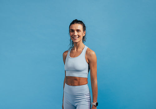 Portrait of young fitness female in sportswear looking at camera while standing on blue background