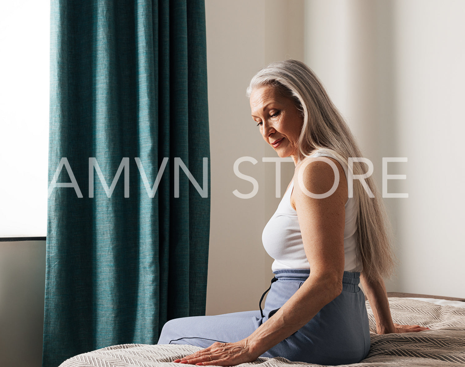 Lonely senior woman in her bedroom. Sad aged woman sitting on a bed and looking down.