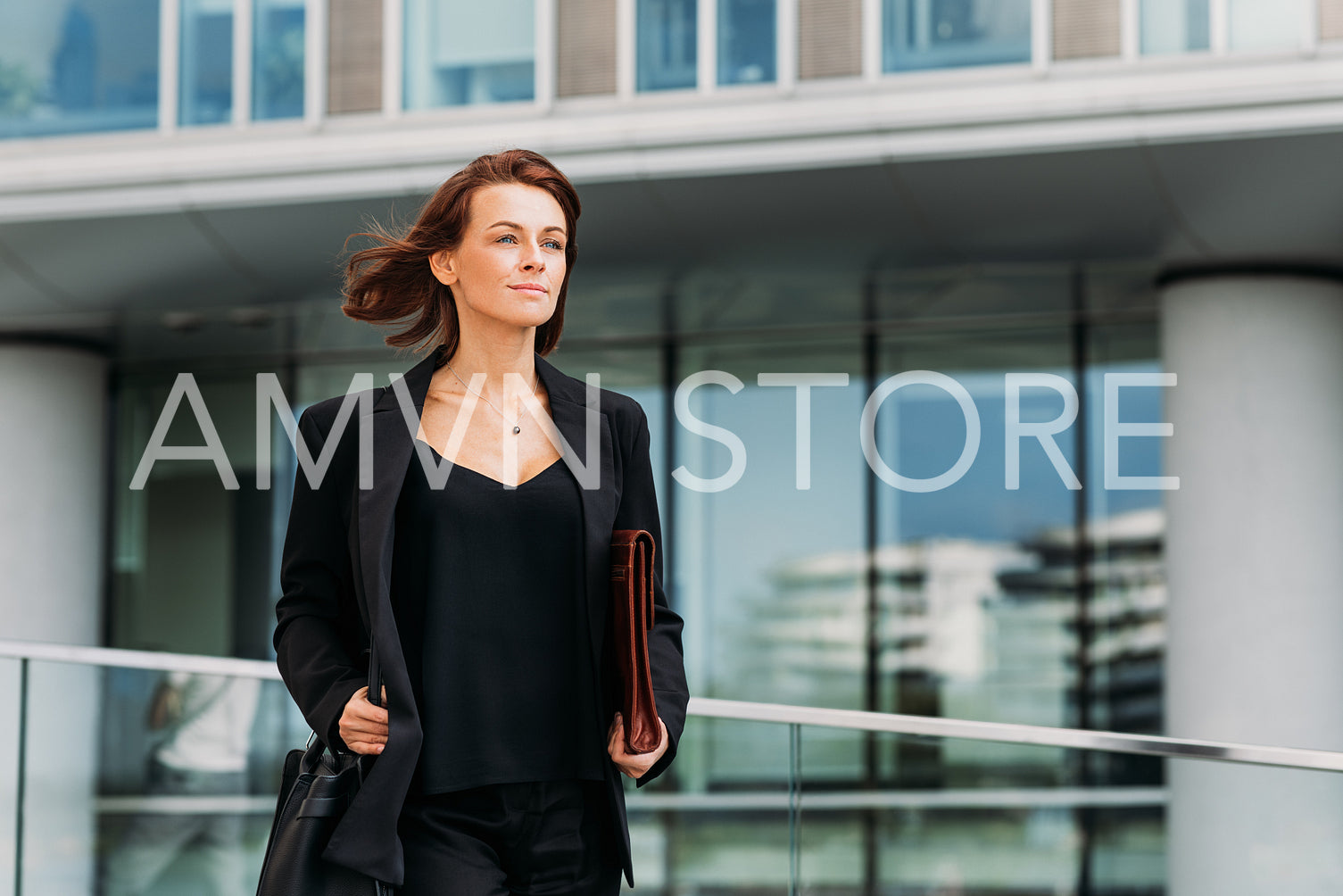 Confident middle-aged businesswoman holding a leather folder walking against an office building