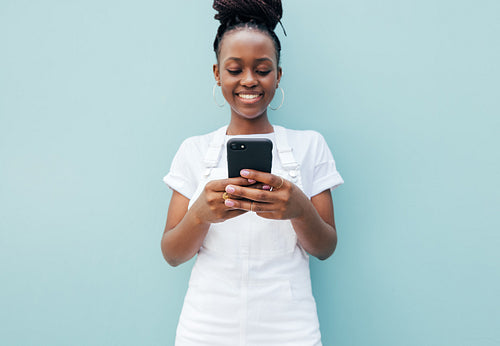 Close up of a positive young female typing on smartphone at blue wall