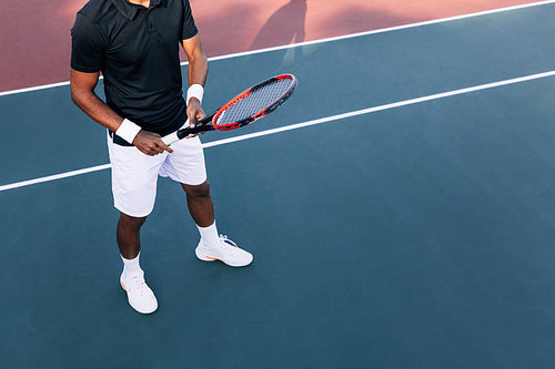 Unrecognizable tennis player in sports clothes standing on a hard court holding a racket