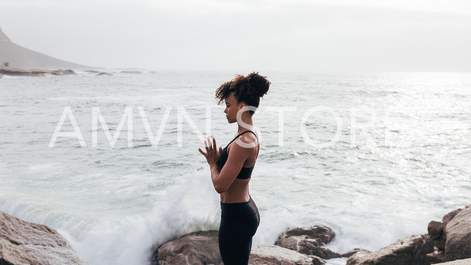 Side view of slim woman in sports clothes praying and meditating by ocean