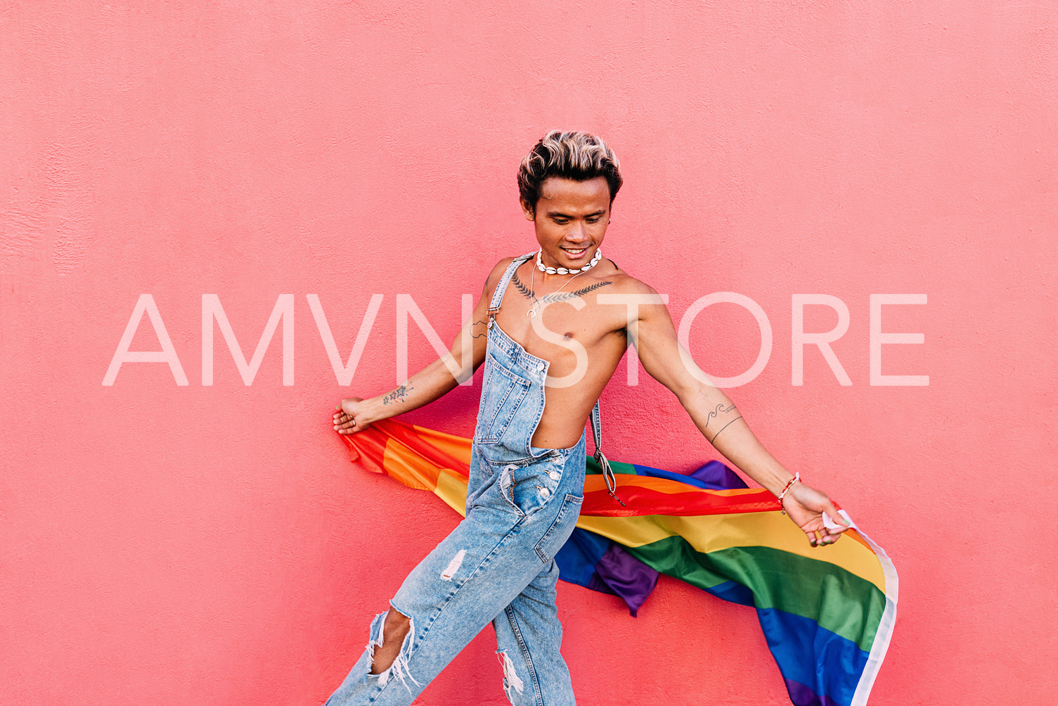 Young guy in denim overalls having fun holding rainbow LGBT flag