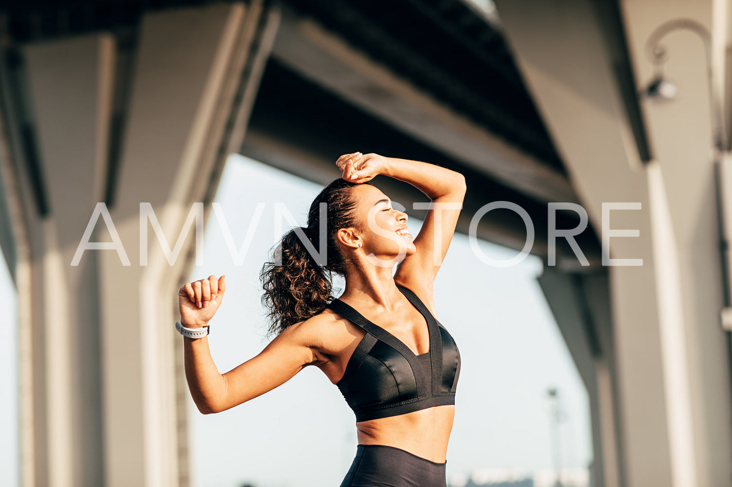 Side view of woman in fitness wears stretching her arms. Smiling female athlete warming up before training outdoors.	