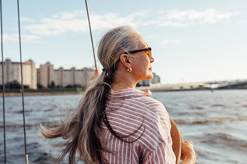 Side view of mature woman wearing sunglasses and looking to the distance while standing on the yacht