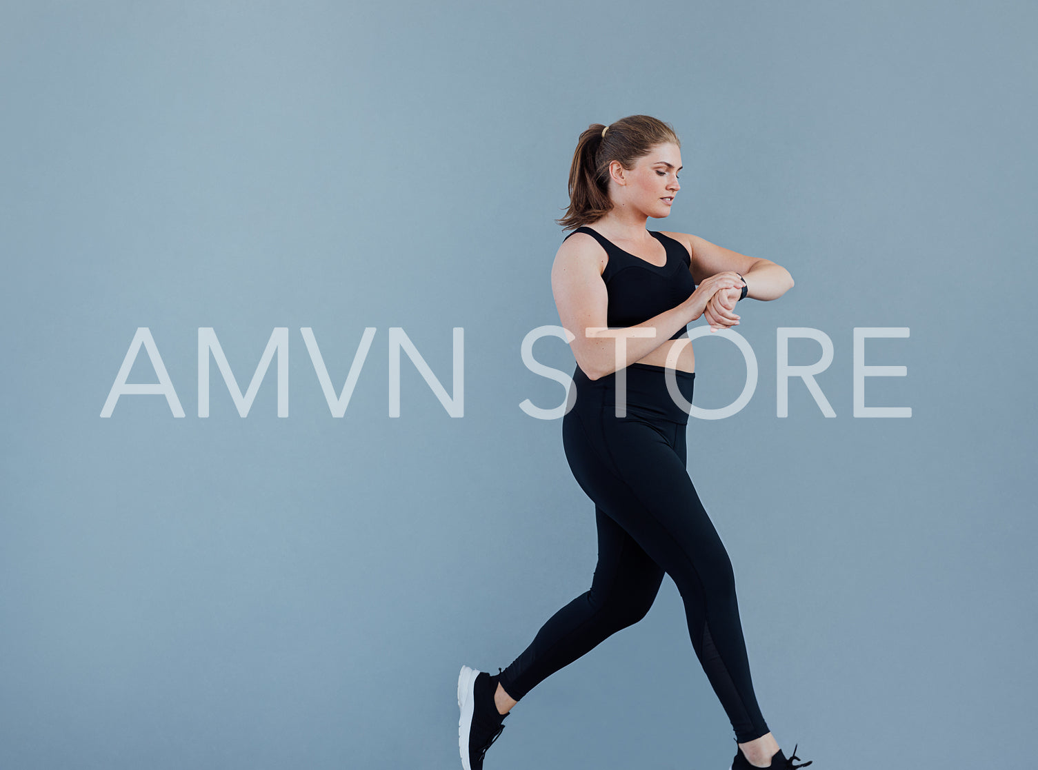 Side view of young plus-size female checking smart watch while jogging at a grey wall. Woman in black sportswear looking at her smartwatch while running.