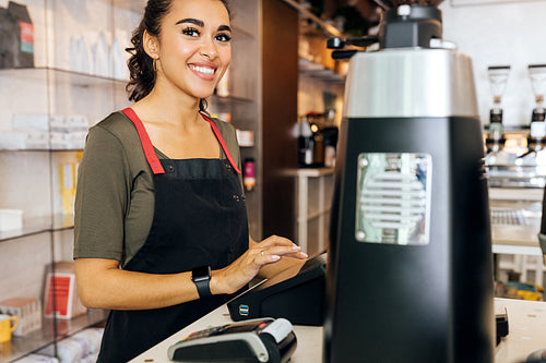 Young beautiful barista standing at counter in cafeteria and looking away