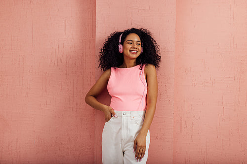 Smiling woman wearing pink headphones looking away leaning on wa