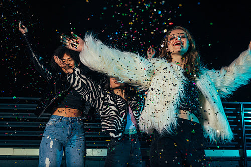 Three happy girls enjoying party. Female friends throwing confetti together and standing under him.