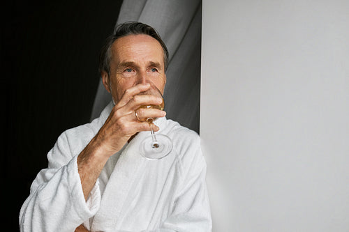 Male relaxing at home. Mature man looking at window and drinking wine.