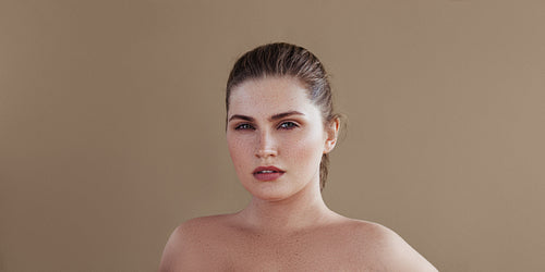 Portrait of a plus size woman posing over pastel backdrop. Young female with smooth skin looking at camera.