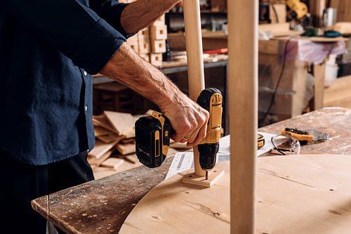 Unrecognizable senior male carpenter drilling a hole in wooden table