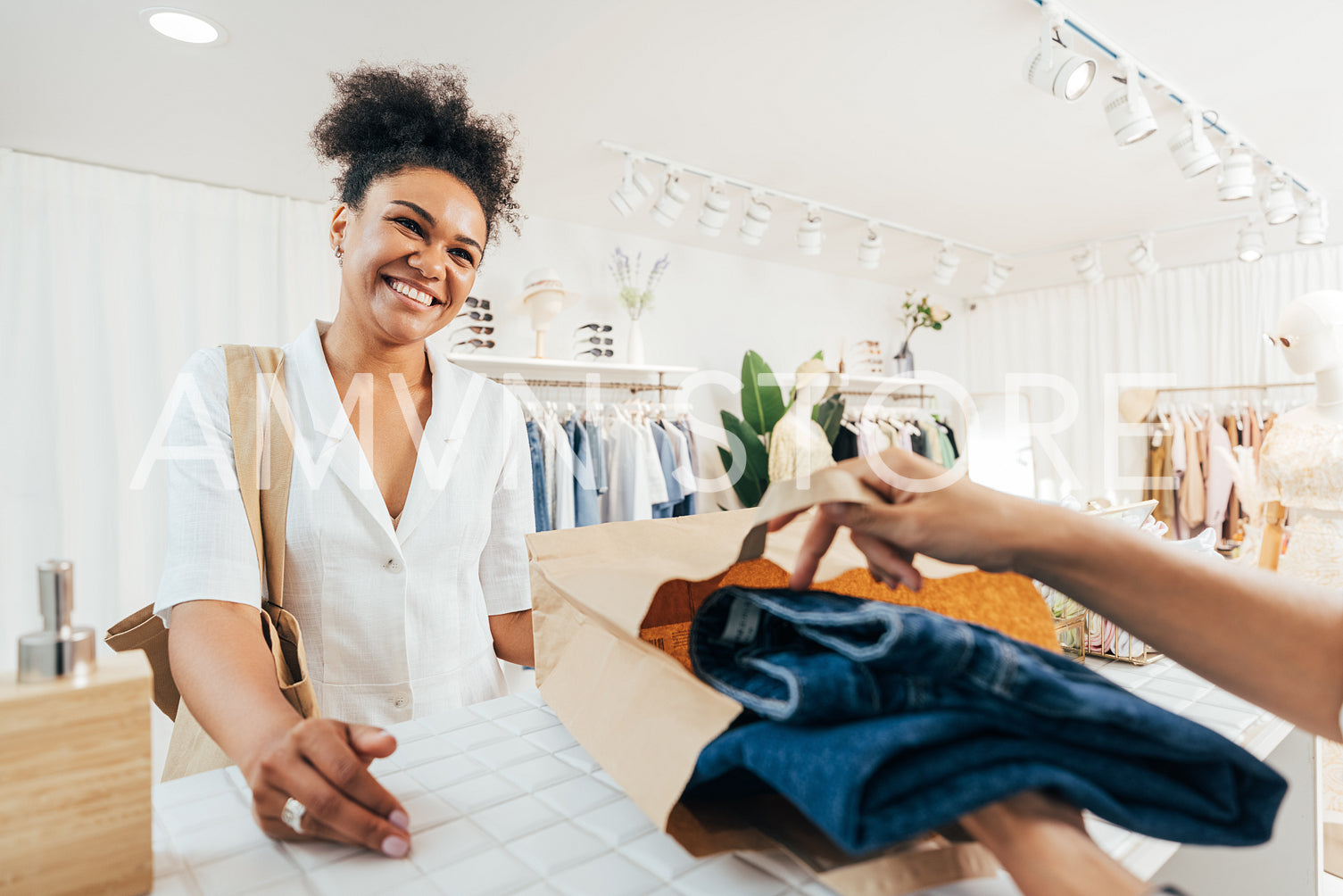 Unrecognizable saleswoman helping customer with purchase. Store owner packing the clothes in a paper bag.