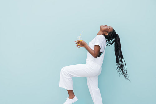 Side view of woman in white clothes having fun against blue wall. Young female holding a juice enjoying good mood.