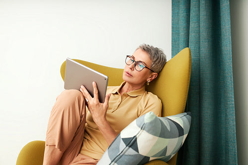 Stylish senior woman relaxing at home reading from digital tablet