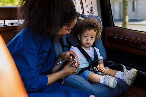 Young mother holding the hand of her son sitting on the backseat of a car