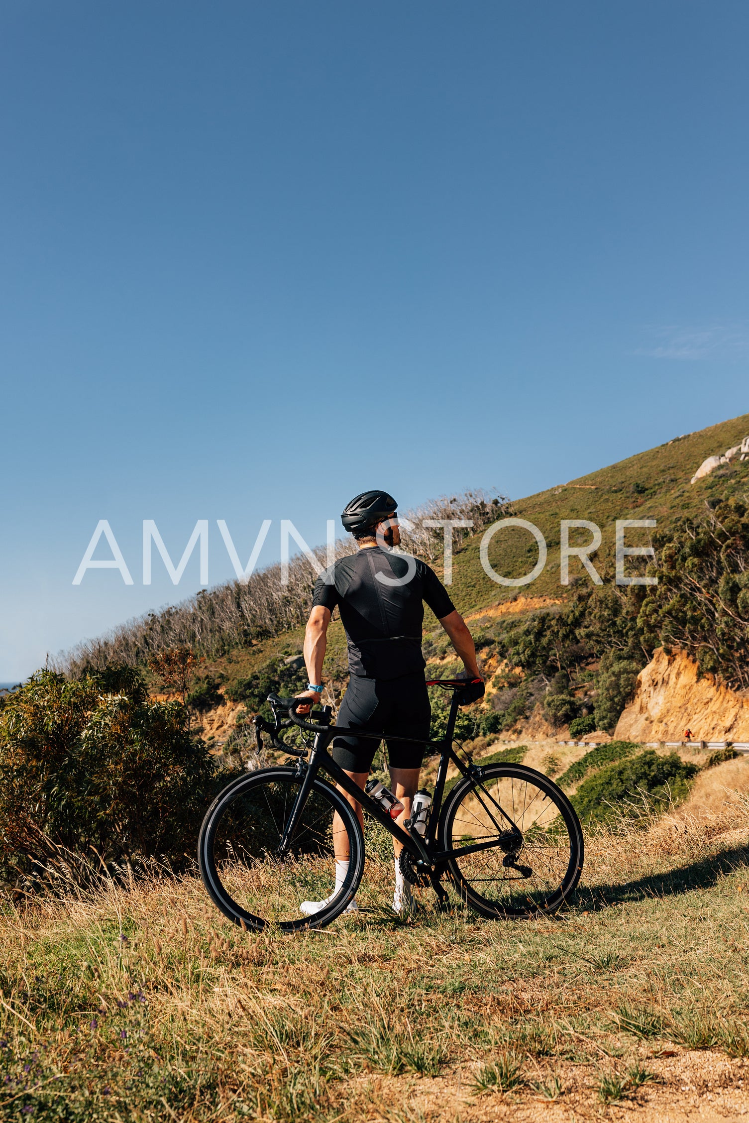 Rear view of a male road bike rider leaning his bicycle while standing in wild terrain