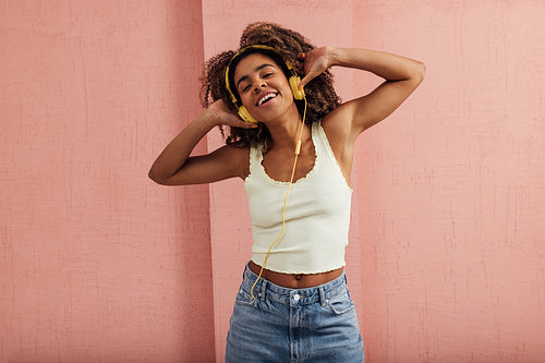 Happy woman enjoying music while standing against pink wall look