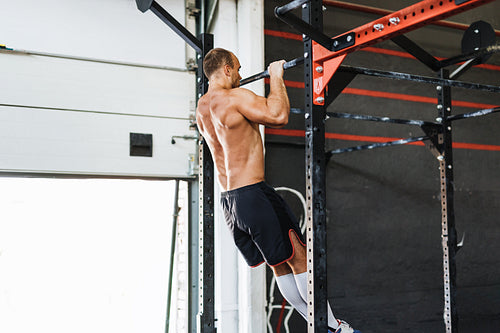 Young bodybuilder doing pull-up workout in gym