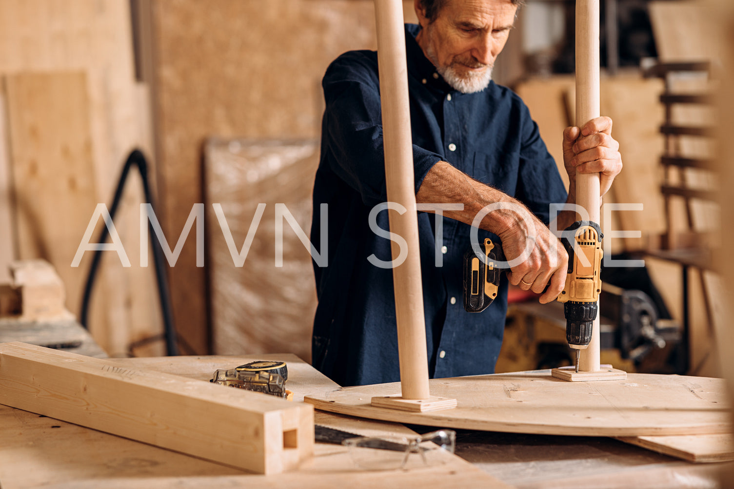 Carpenter repairing legs of a table with electric drill in his workshop	