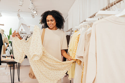 Young stylish woman standing in small boutique looking at dress she choose