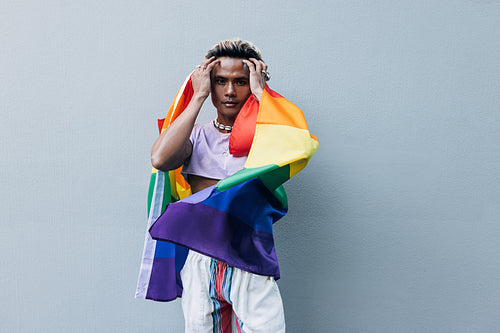 Young stylish guy adjusting his hair while standing outdoors with rainbow lgbt flag