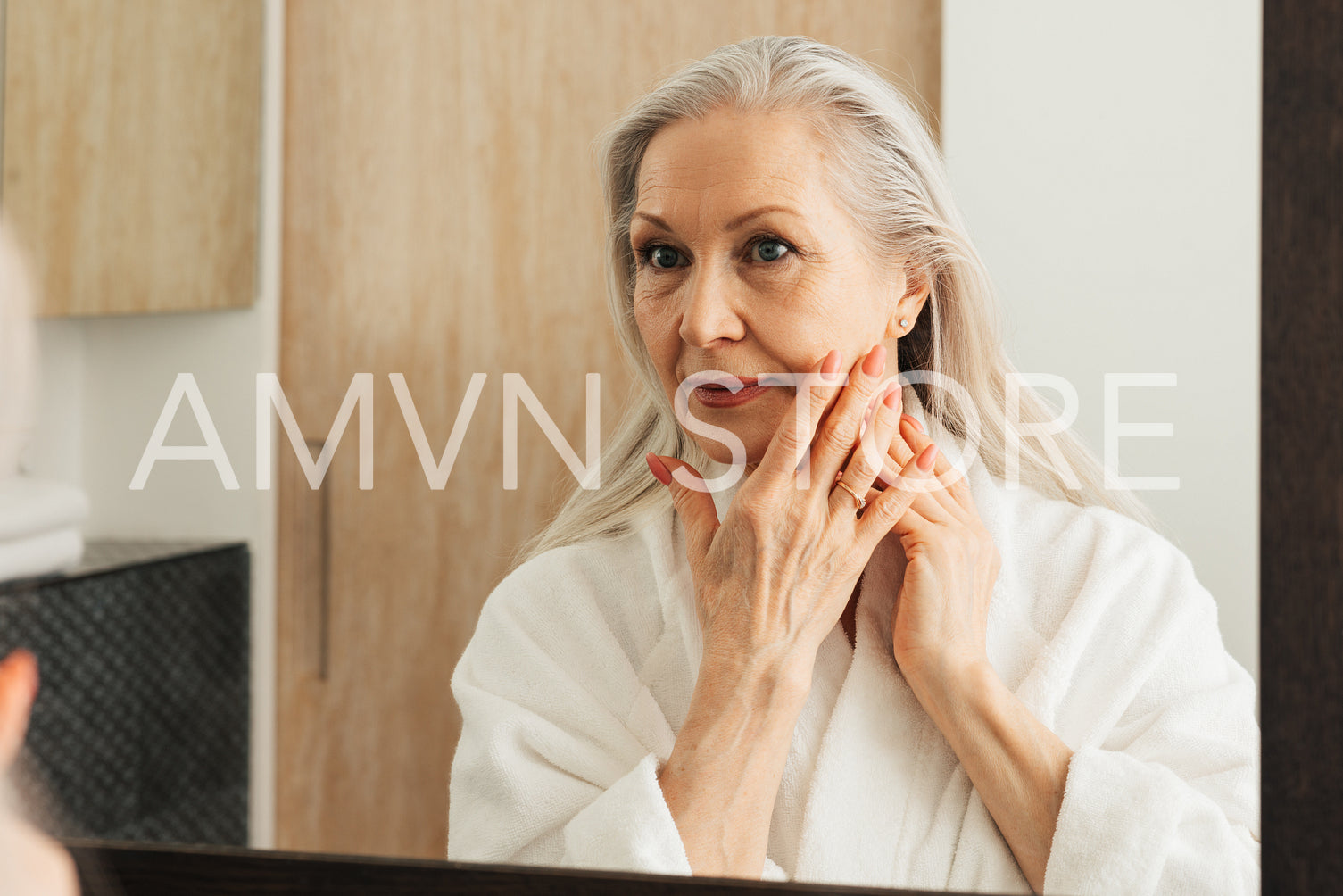 Senior woman with long grey hair touching her cheek with fingers in bathroom