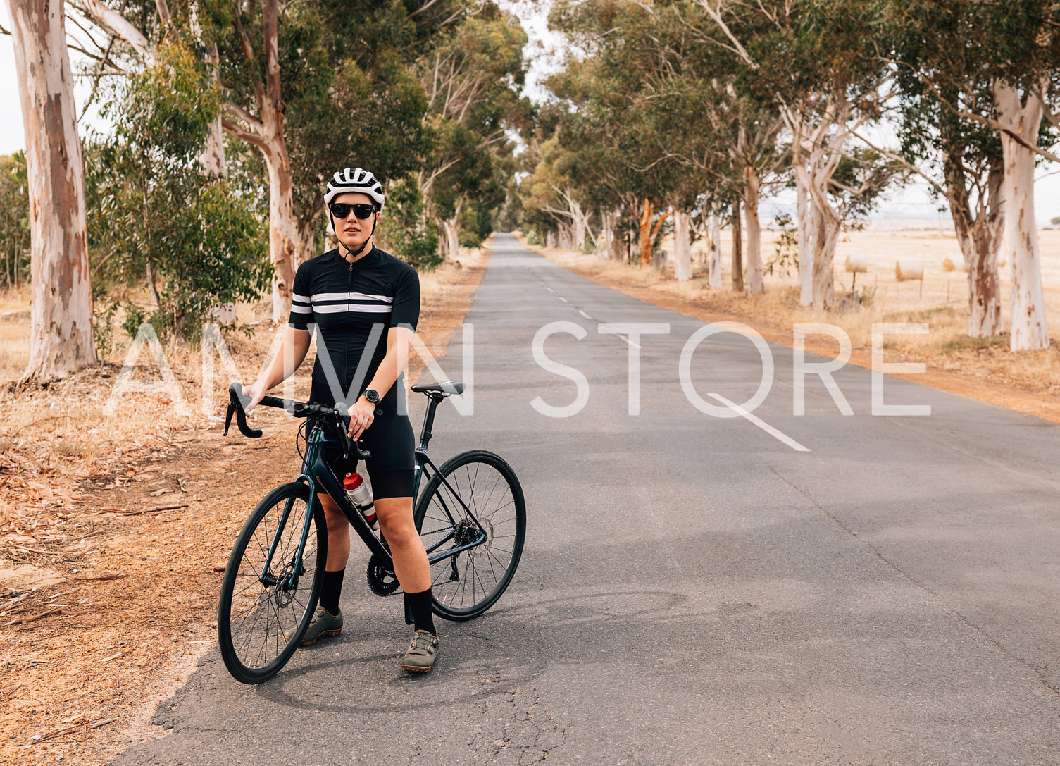 Professional female cyclist taking a break on a long empty countryside road