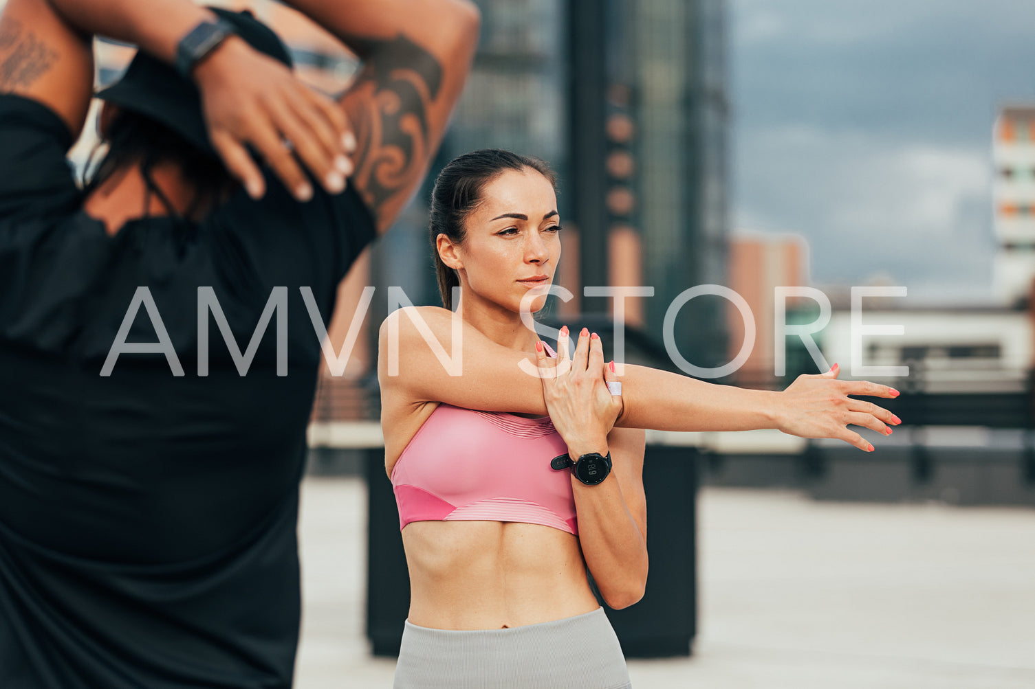 Two athletes are exercising on a rooftop. Young female stretching her arm before training.