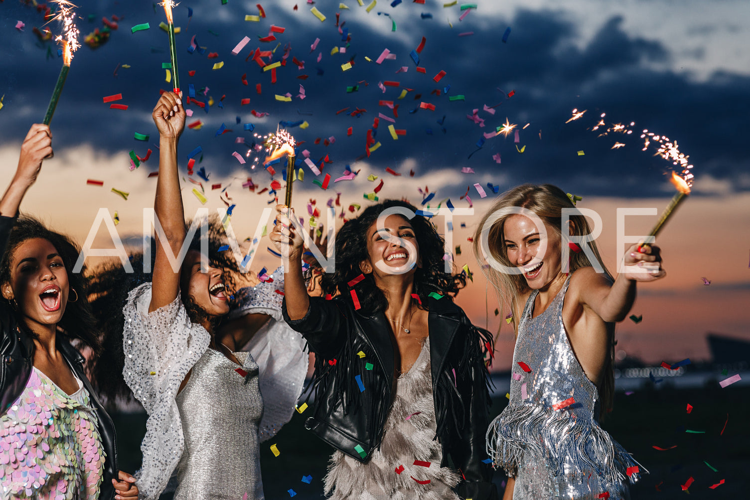 Group of four happy women dancing with sparklers under confetti at sunset	