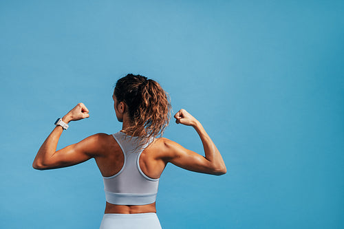 Rear view of young woman showing her biceps on blue background w