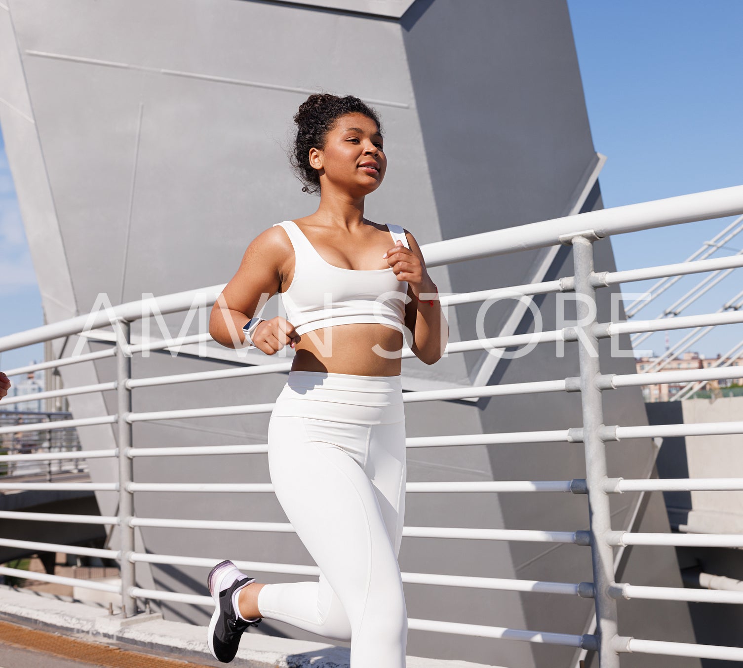 Young woman in white sportswear running outdoors on bridge. Female in white fitness attire jogging during a sunny day.