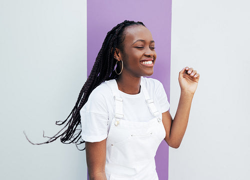 Young smiling female enjoying a good mood. Happy woman in white overalls standing at the wall.