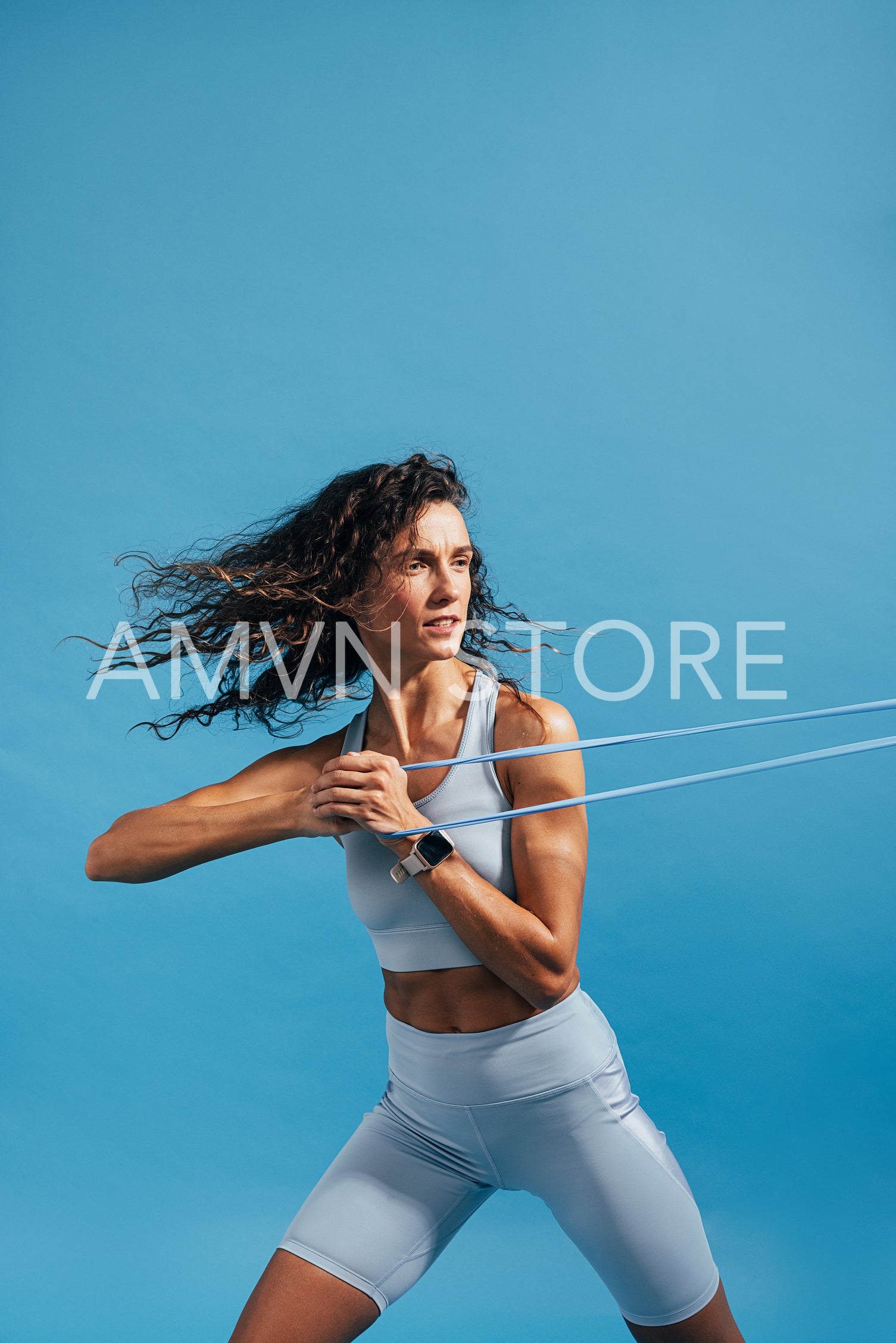 Muscular woman exercising against blue background using resistance bands. Fitness female doing strength workout.