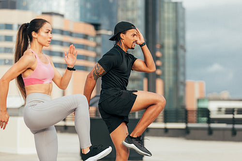 Young athletes are exercising together on rooftop. Man and woman are warming up before training outdoors.