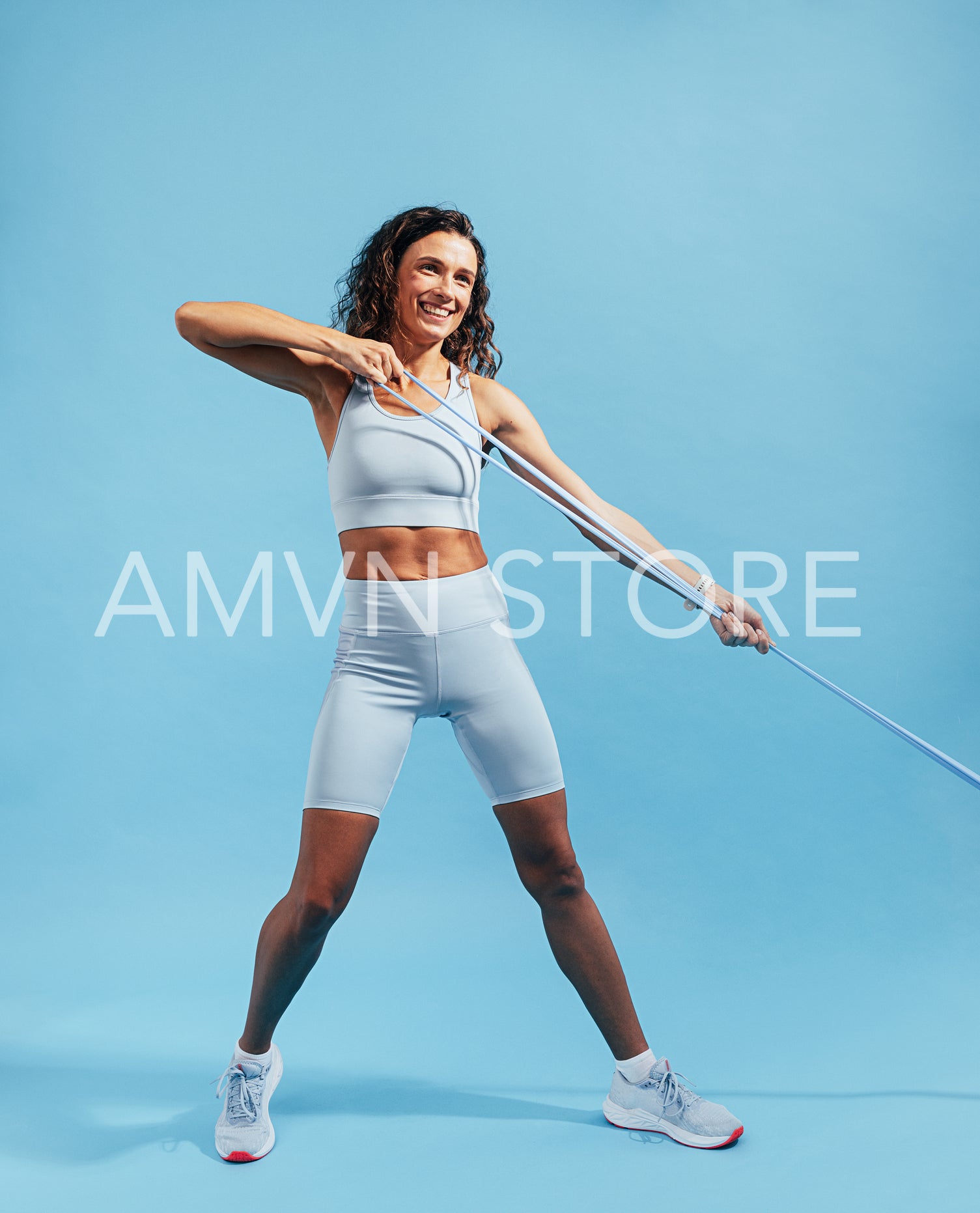 Smiling woman exercising with elastic training band against a blue background