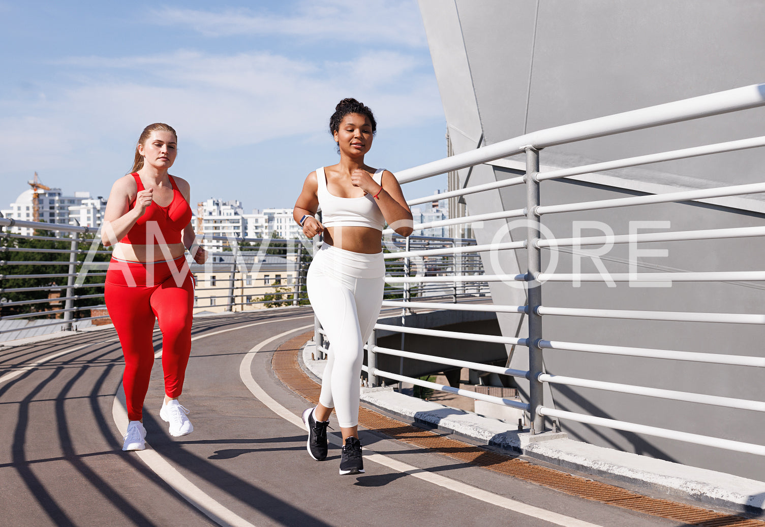 Two females in sportswear with different color running on bridge at sunny day