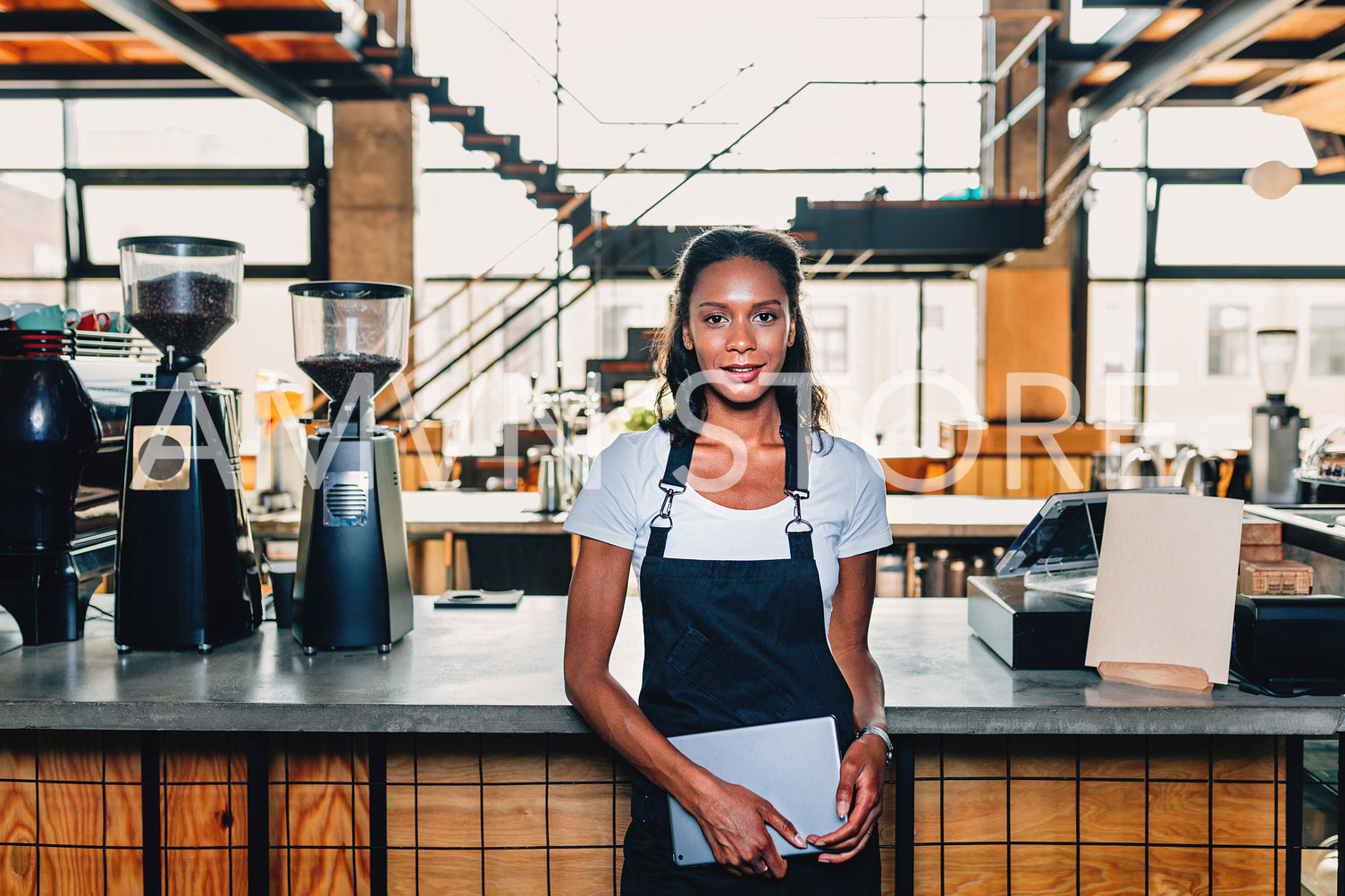 Young woman leaning on the counter at her coffee shop	