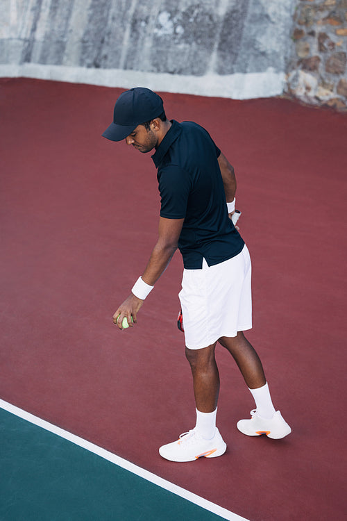 Young man bouncing the ball at the baseline on the hard court for the serve