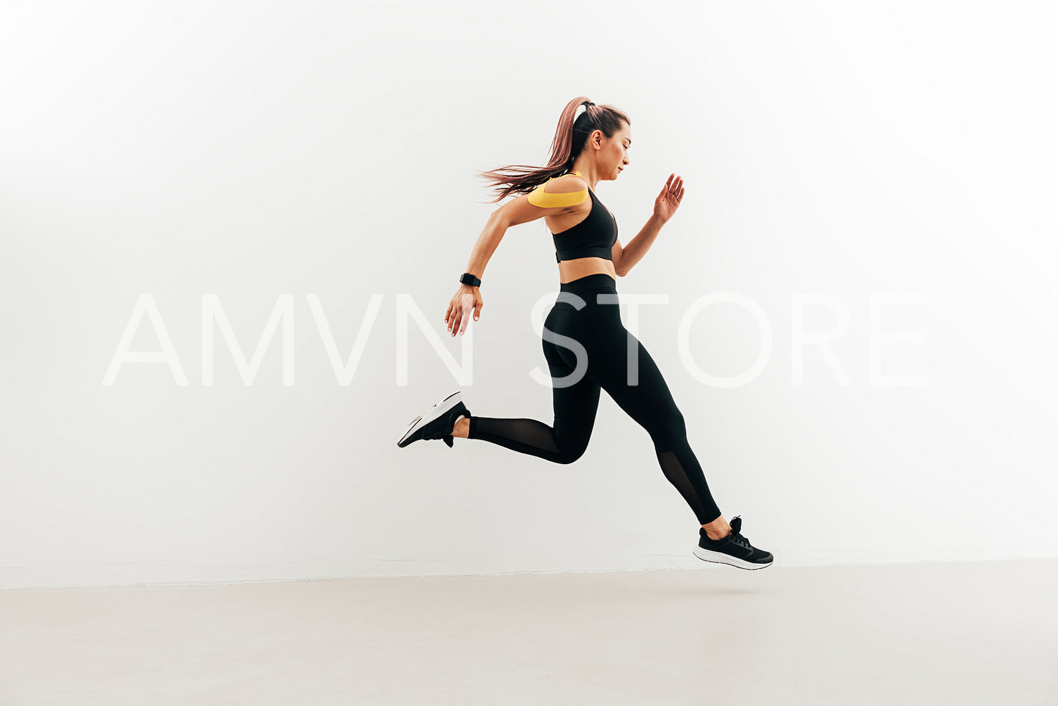 Runner in sport clothes sprinting near a white wall. Woman with kinesiology tape on shoulder jogging indoors.