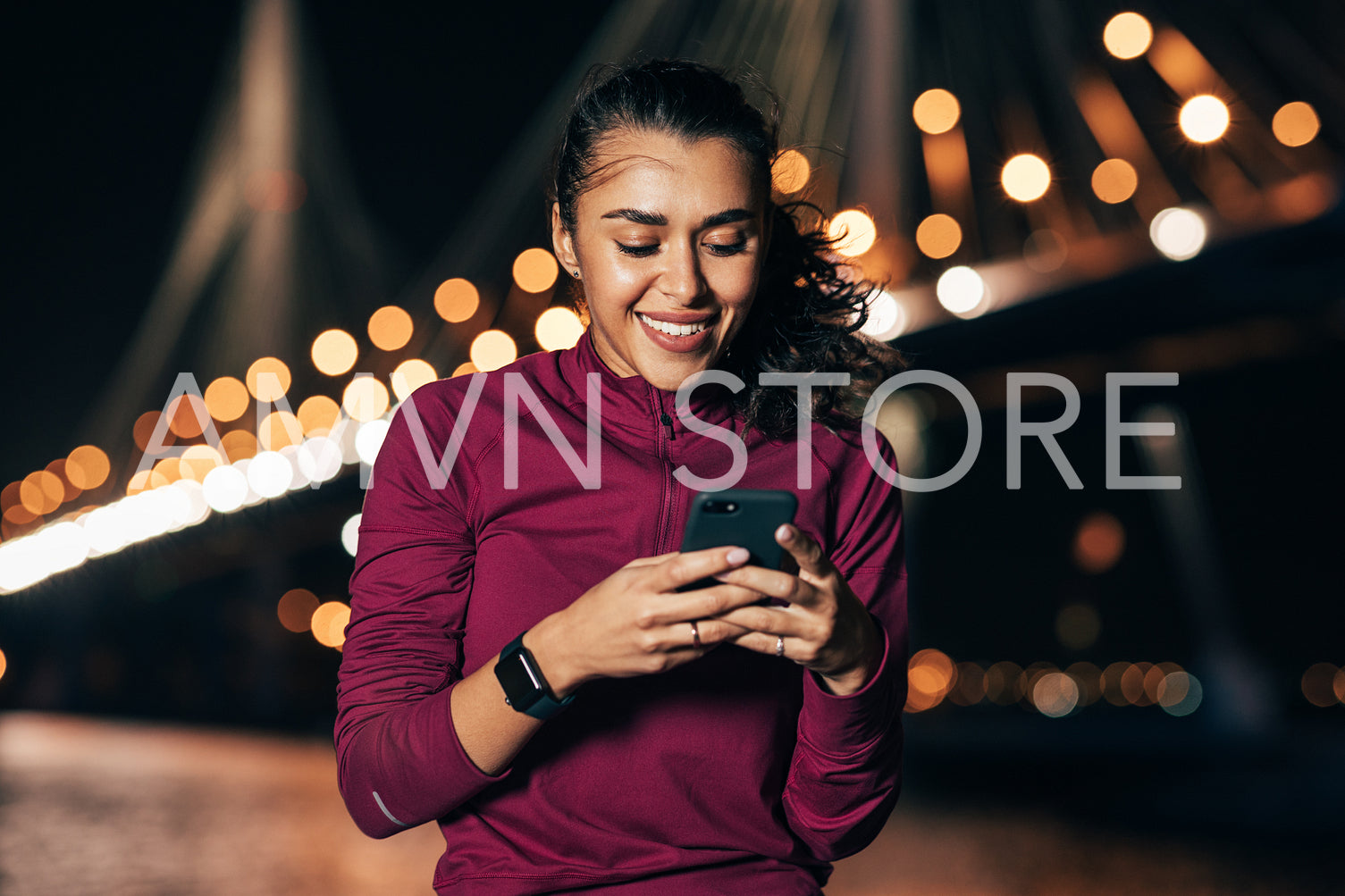 Young female in sportswear typing on smartphone while sitting at night outdoors