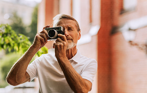 Portrait of a senior photographer taking photographs with an analog camera outdoors