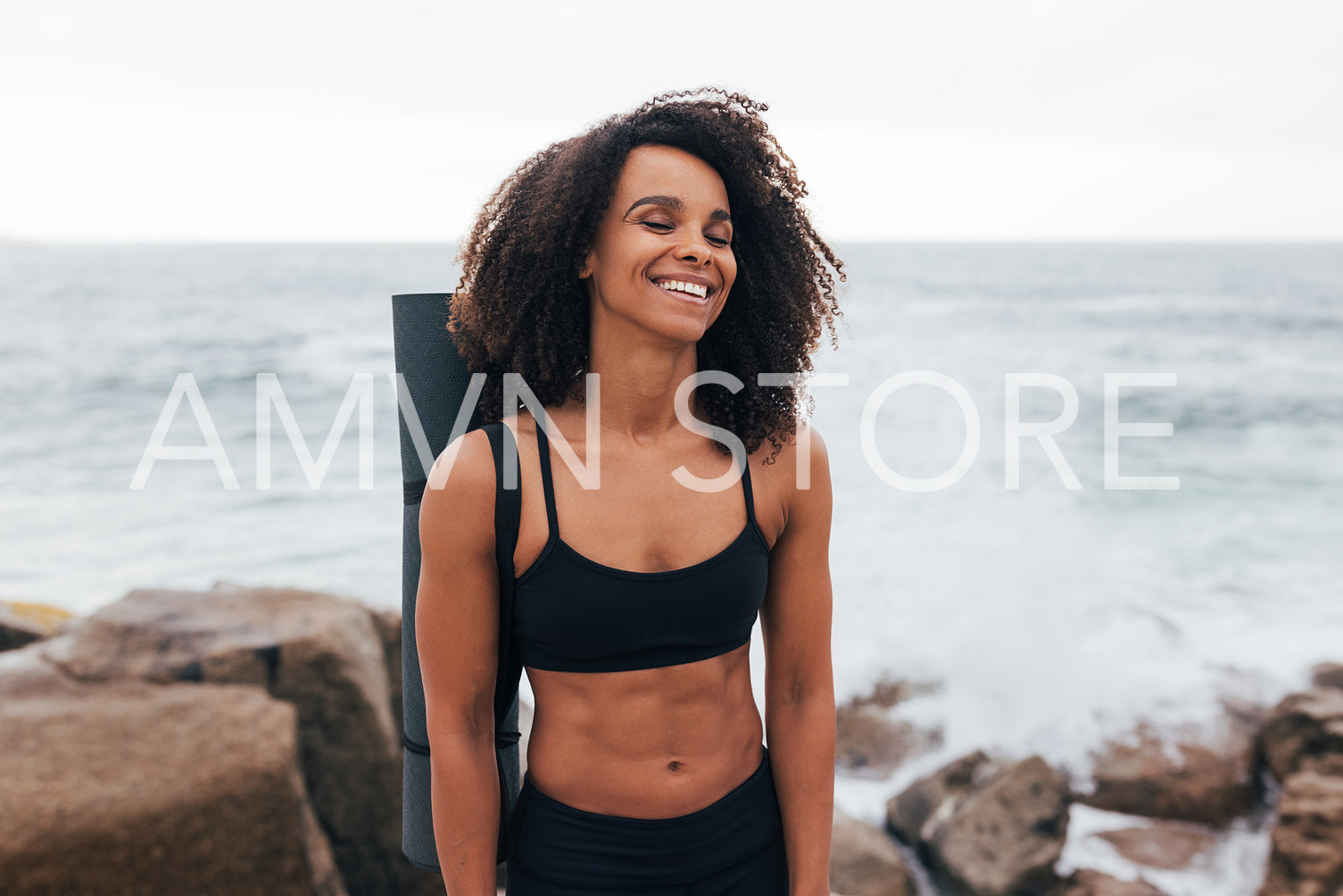 Laughing woman with closed eyes standing by the ocean after yoga training